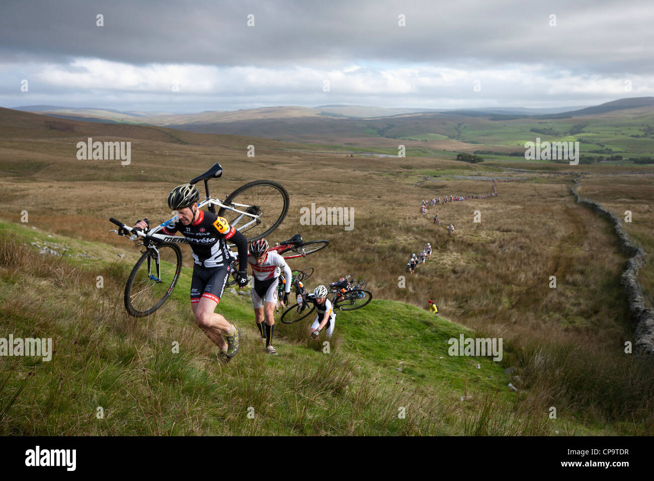 Les cyclistes portent leurs bicyclettes d'une côte raide pendant les trois sommets Cyclo-Cross dans Yorkshire du Nord, Angleterre, Royaume-Uni Banque D'Images