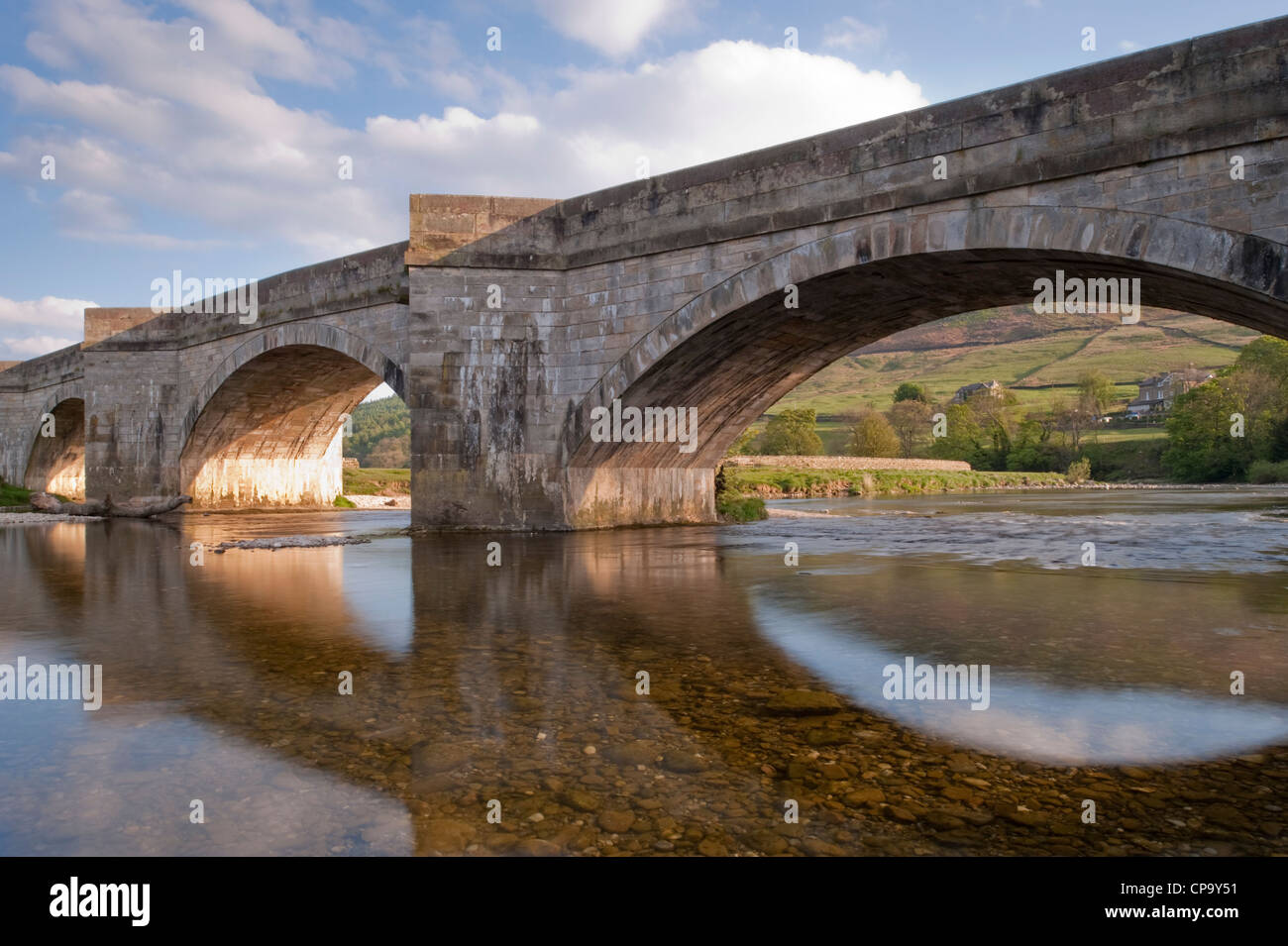 Soirée ensoleillée, vue sur la rivière du vieux pont voûté en pierre, reflétée dans les eaux peu profondes, l'eau claire de la rivière Wharfe, Tonbridge, Yorkshire, Angleterre, Royaume-Uni. Banque D'Images