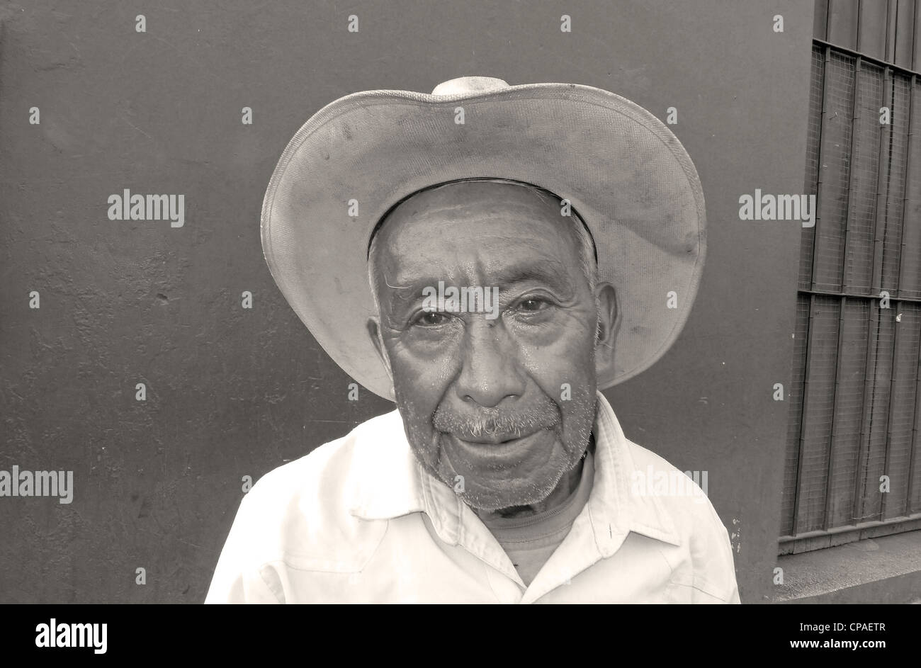 Guatemala Antigua smiling man with cowboy hat sitting par colorful wall scène de rue pavées site de l'Unesco Banque D'Images