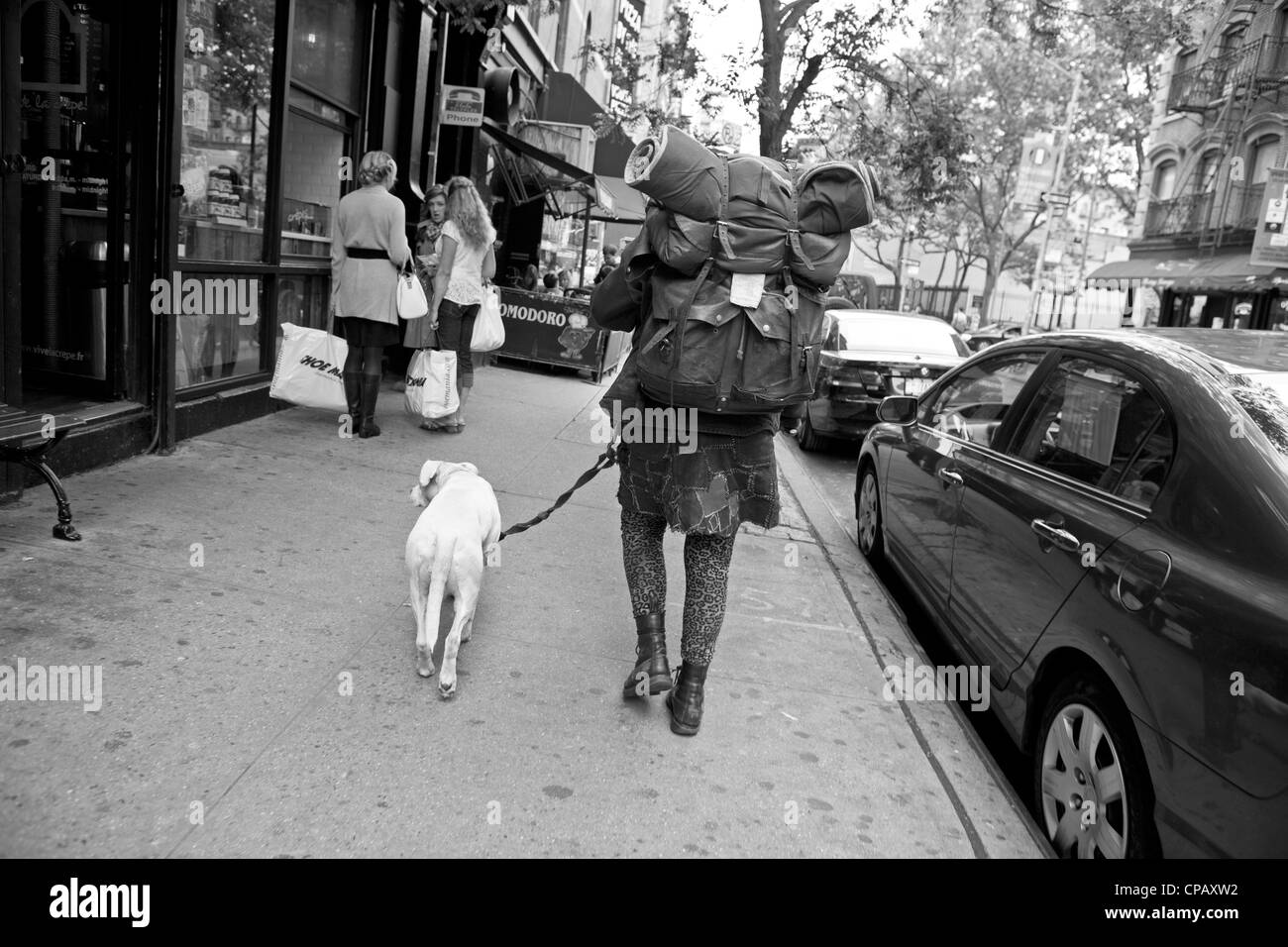 Une femme sans-abri promenades son chien sur le trottoir à New York City. Banque D'Images