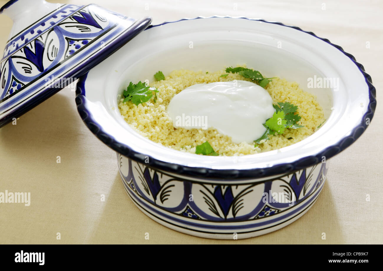 L'Afrique du nord un tajine en poterie bowl full of couscous, surmontées de yaourt frais et garnie de feuilles de coriandre Banque D'Images