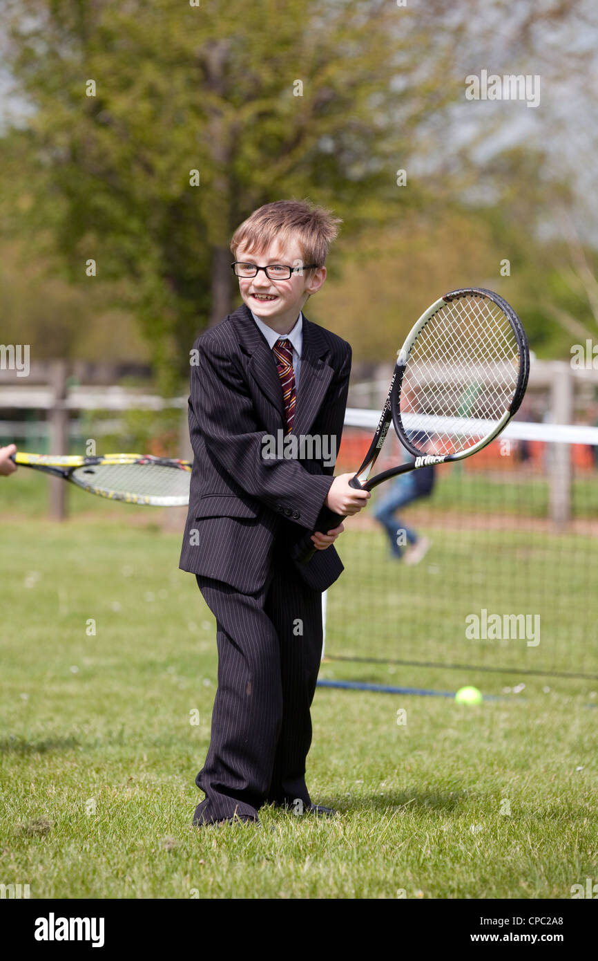 Plutôt comique vu de jeune garçon en costume et cravate en jouant au tennis, sports Newmarket Suffolk festival UK Banque D'Images