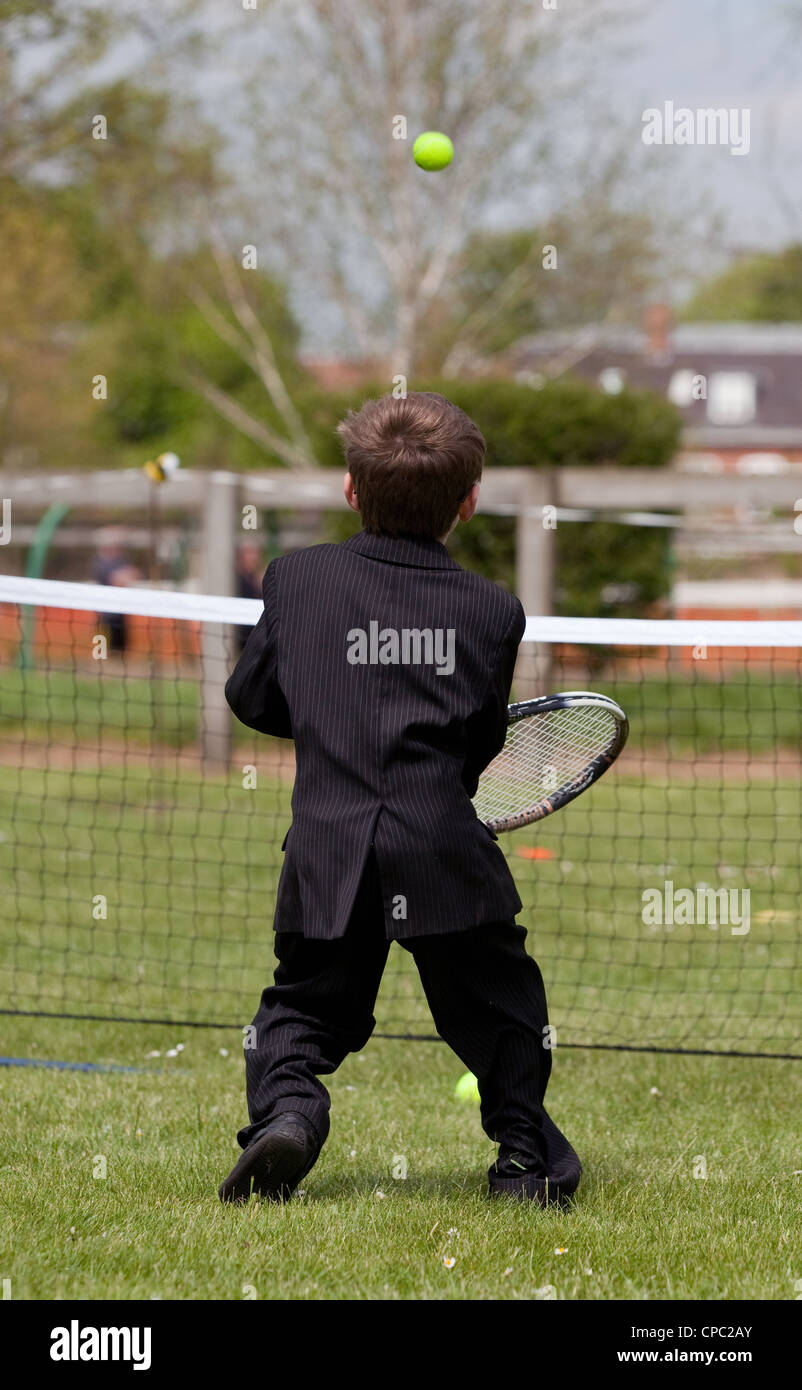 Vue arrière d'un jeune garçon vêtu d'un costume d'essayer de jouer au tennis, Newmarket Suffolk, UK sports Festival Banque D'Images