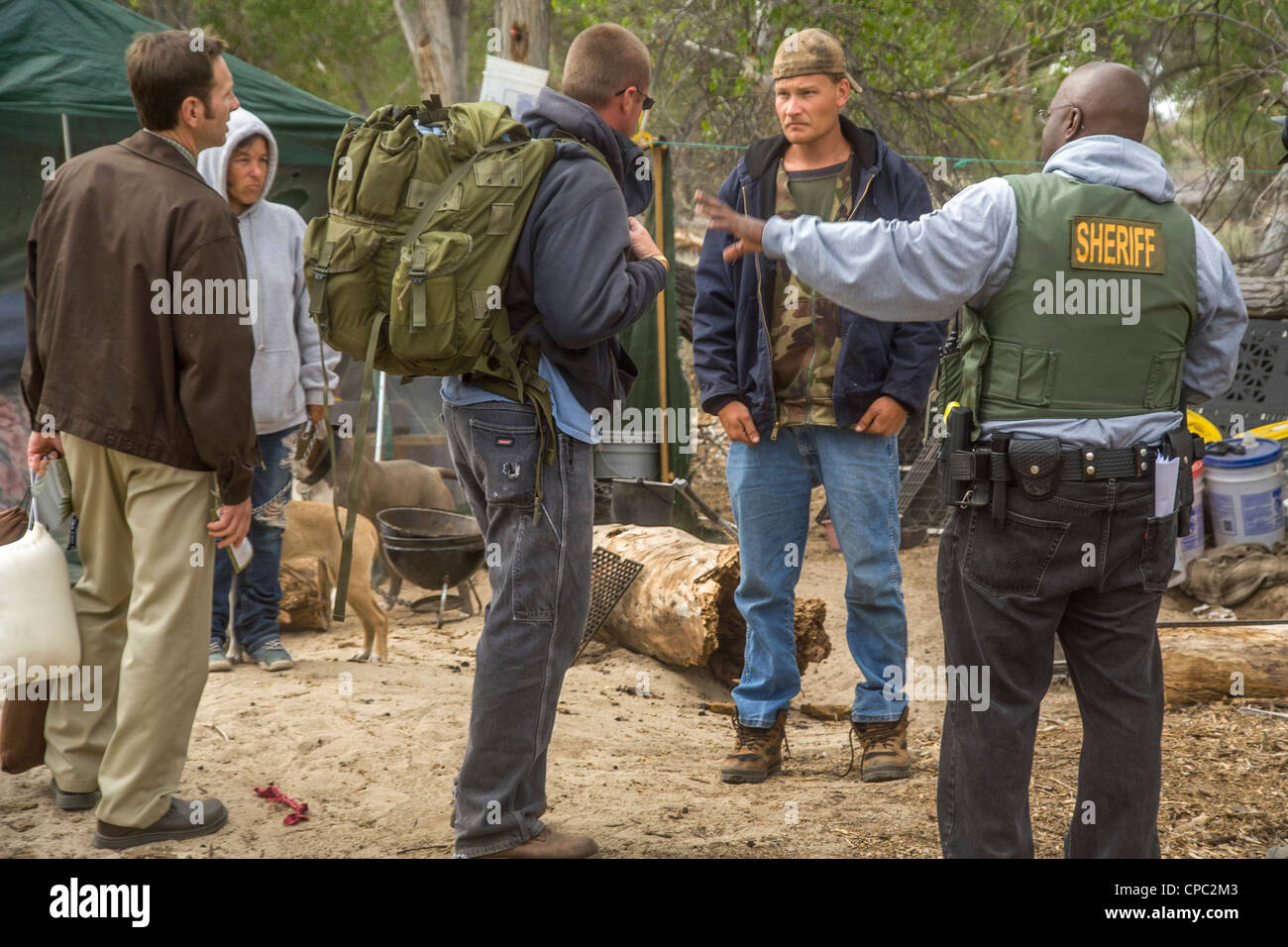Un ministre et un adjoint du shérif rencontrez un couple de sans-abri et leurs chiens vivant dans une cabane et une vieille tente dans le désert. Banque D'Images