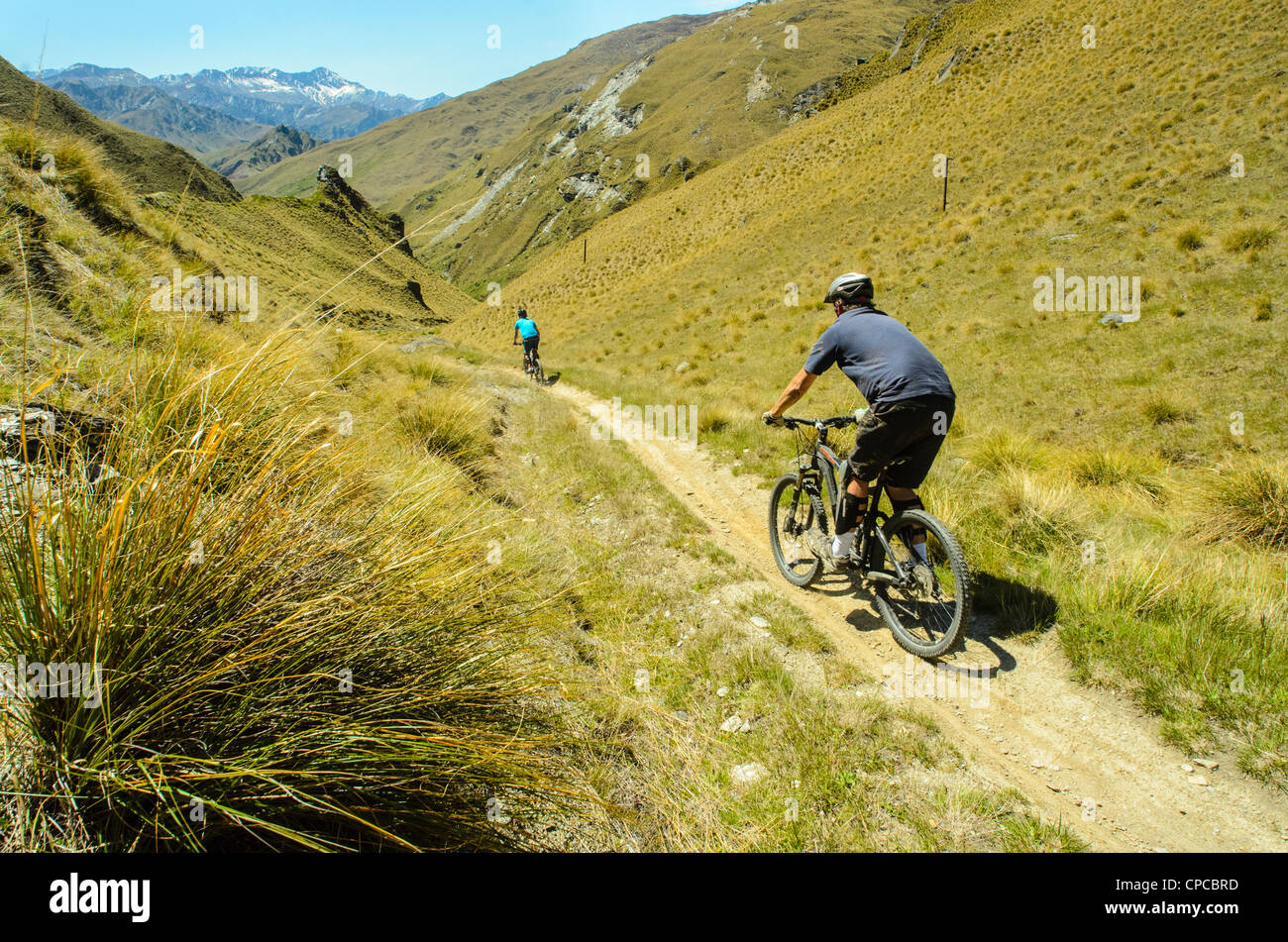 Les vététistes descendant le pack piste, Skippers Canyon, près de Queenstown, avec Mt Aurum sur l'horizon, Nouvelle-Zélande Banque D'Images