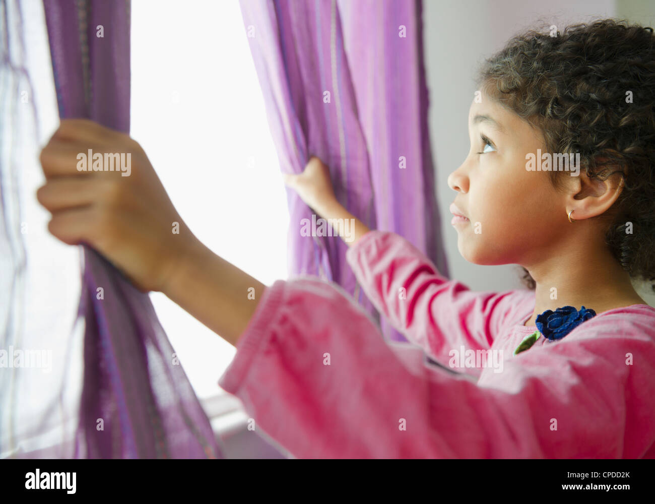 Mixed Race girl opening curtains Banque D'Images