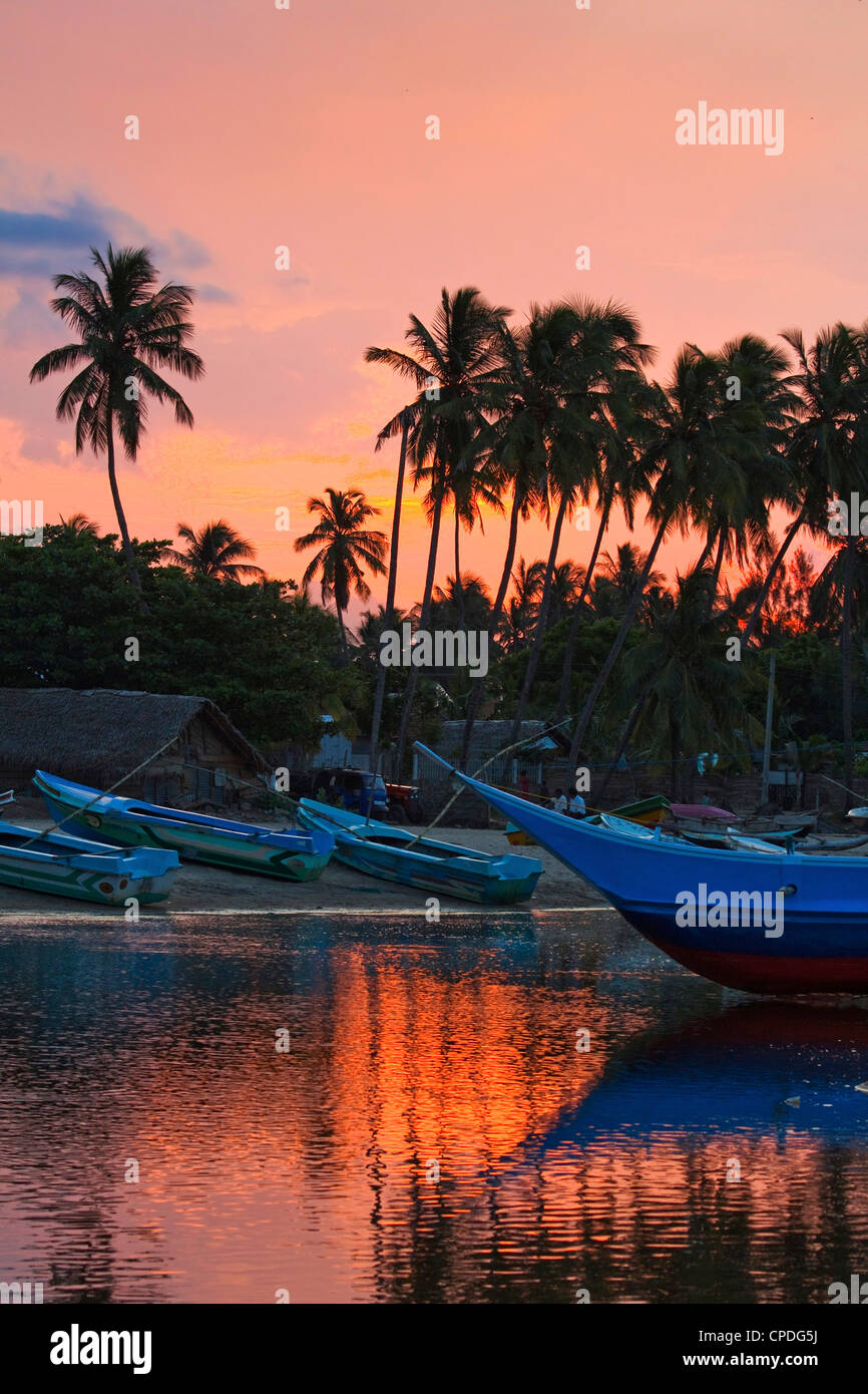 Des bateaux et des palmiers au coucher du soleil à cette pêche à la plage et surf spot touristique populaire, d'Arugam Bay, Province Orientale, au Sri Lanka Banque D'Images
