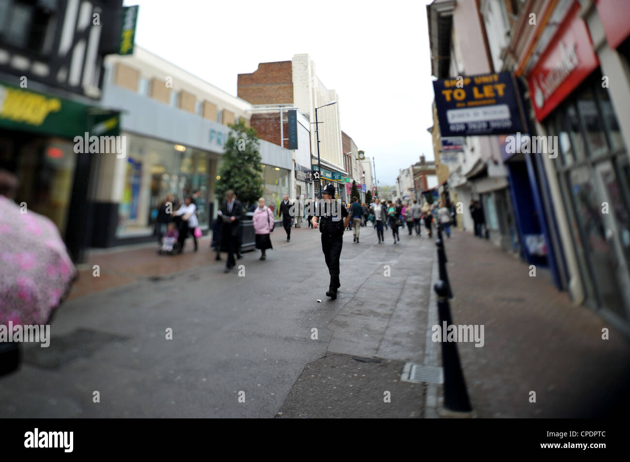 Un policier marche sur une rue commerçante animée en Angleterre. Semaine St, Maidstone, Perspective de l'objectif de contrôle donne à faible profondeur de fiel Banque D'Images