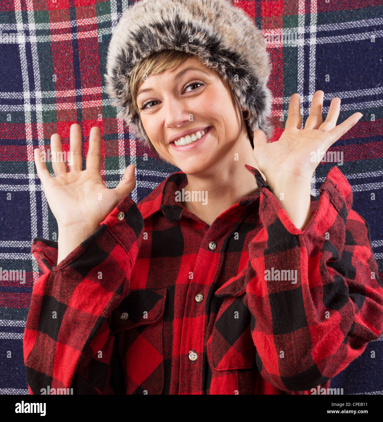Smiling young woman wearing bûcheron à carreaux chemise et fur hat forme à deux mains à l'appareil photo. Funny studio shot Banque D'Images