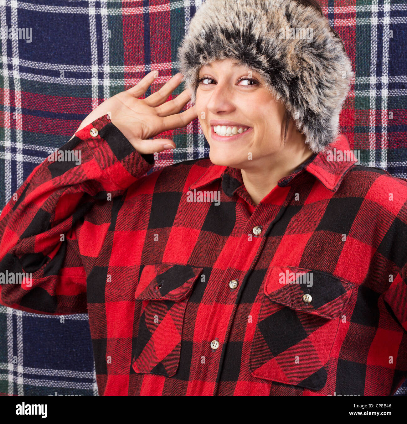 Souriante jeune femme portant chemise bûcheron et fur hat posing et forme avec sa main à l'appareil photo. Funny studio shot Banque D'Images