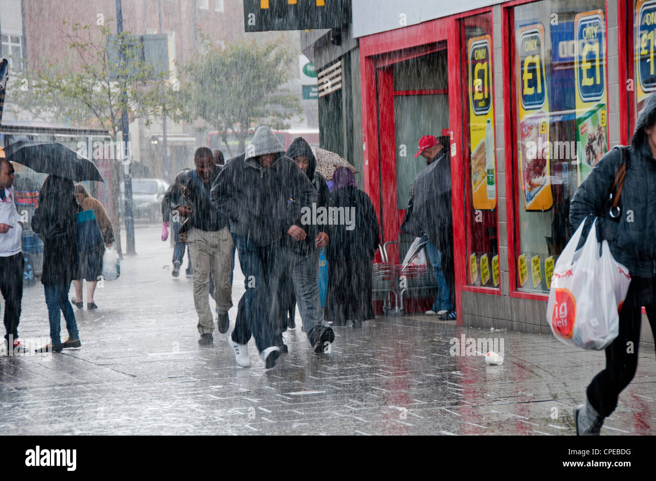 Les gens se précipiter à travers des rues de Lewisham en tempête avec parasols Banque D'Images