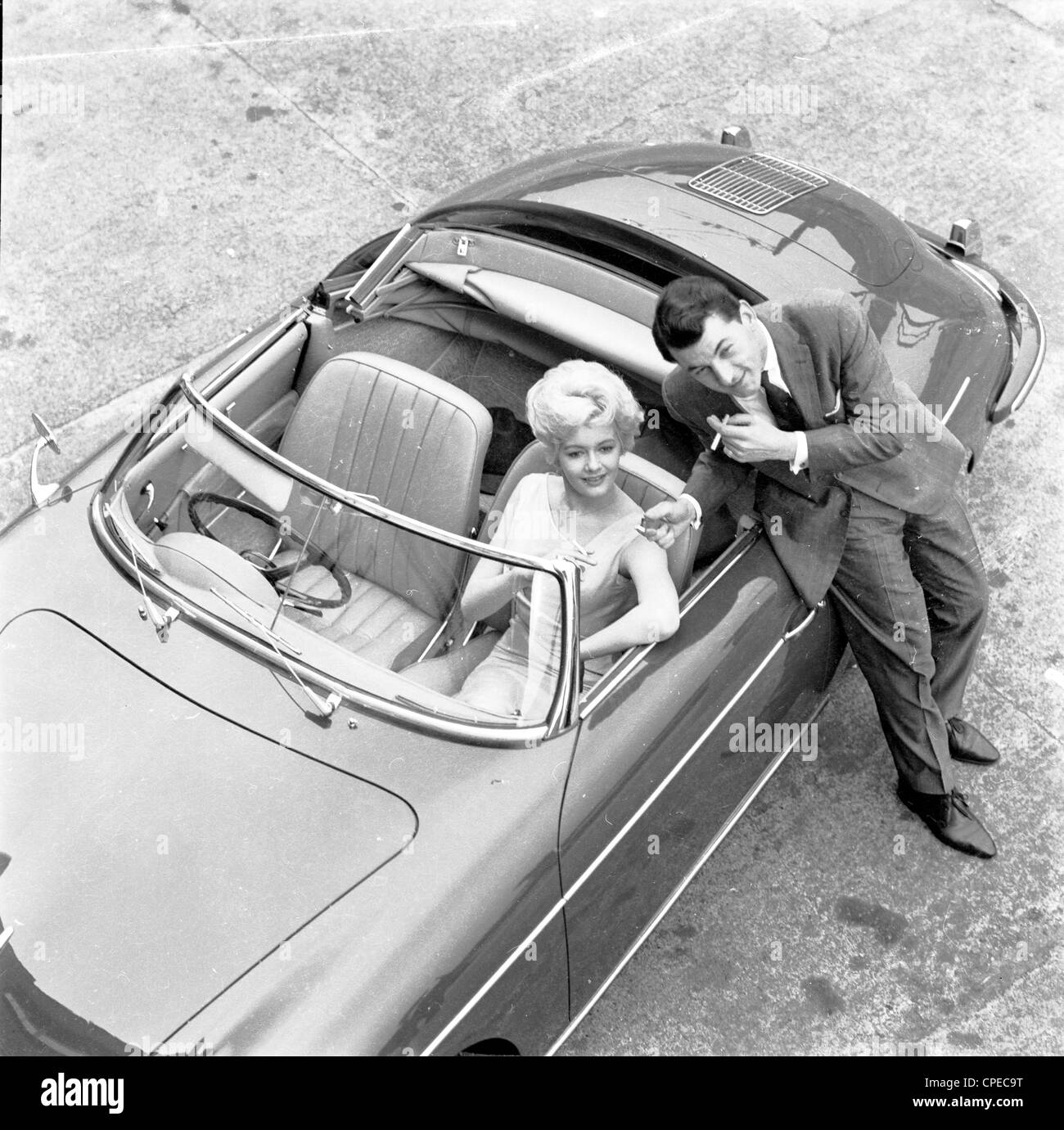 Années 1960. Quelques photos de couple et par une voiture de sport à toit ouvert, l'homme de fumer une cigarette. Banque D'Images