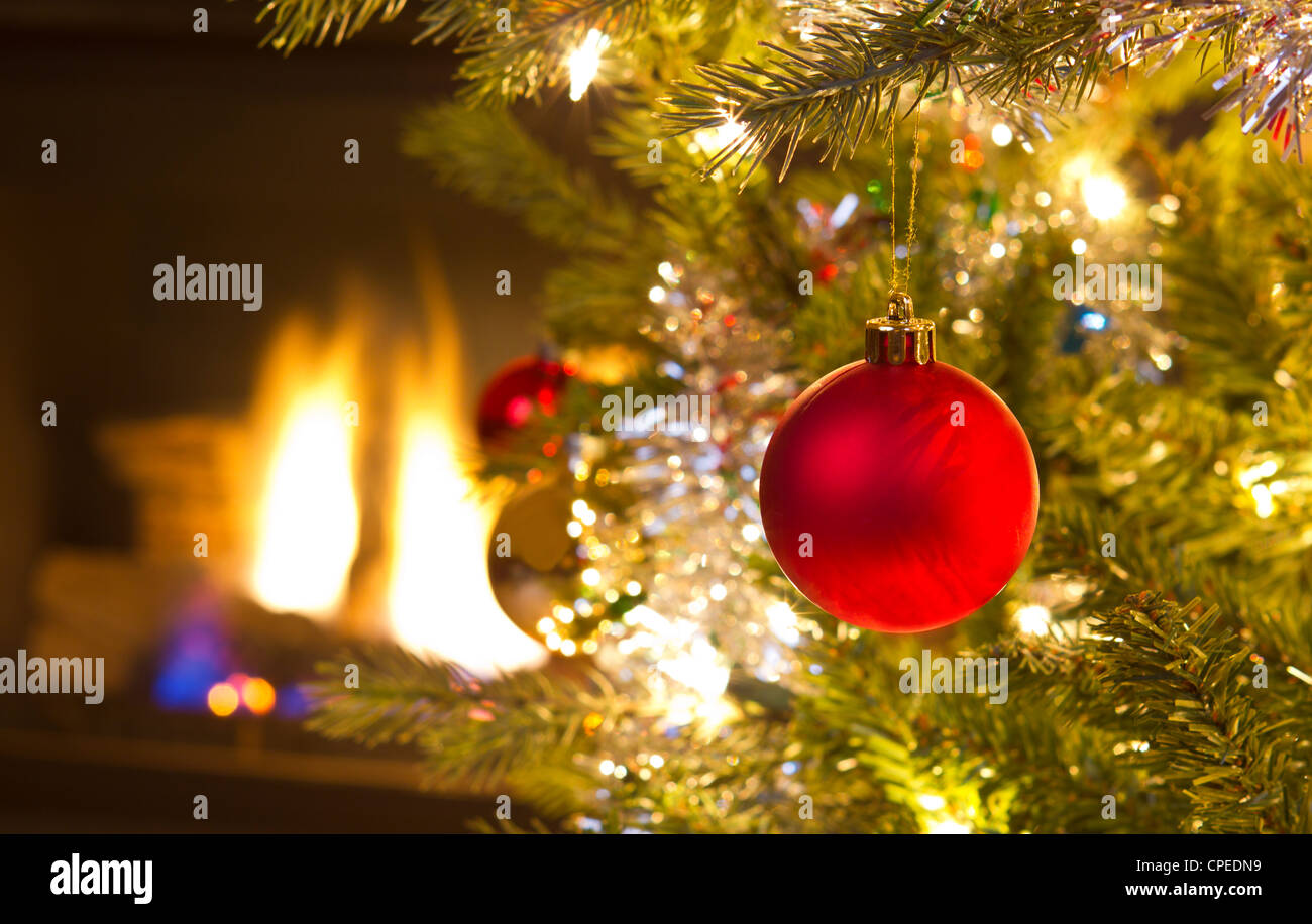 Bright red Christmas ornament hanging sur arbre de Noël avec cheminée en arrière-plan Banque D'Images