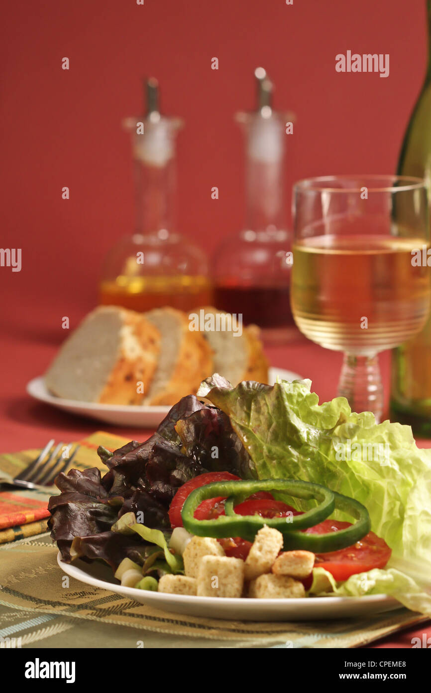 Un lieu de réglage avec salade de laitue pain au levain, et un verre de vin, avec de l'huile et vinaigre huilier rond sur un fond rose. Banque D'Images