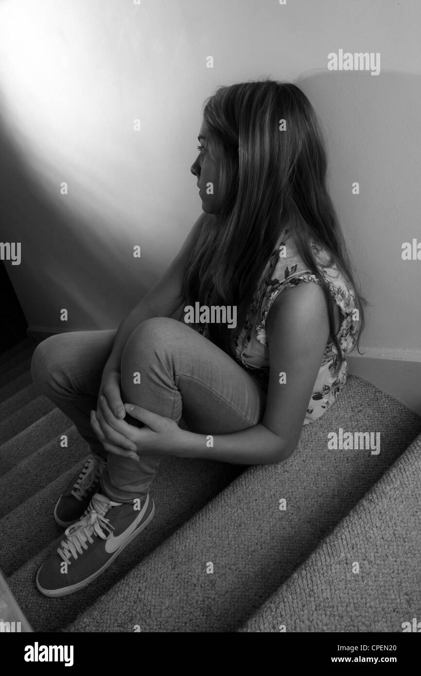 Jeune fille assise sur un escalier sombre vue arrière Banque D'Images