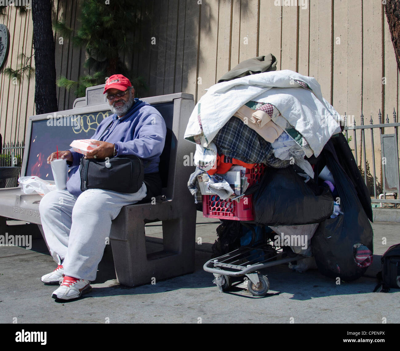 Les sans-abri à Los Angeles. Photo d'un grand homme assis sur un banc d'arrêt de bus avec biens empilés sur un panier. Banque D'Images