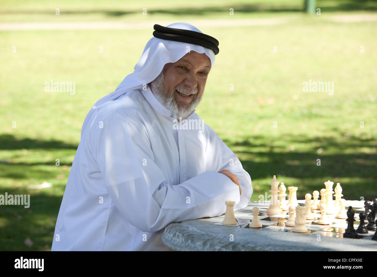 Portrait d'un homme arabe senior jouant aux échecs dans le parc, en souriant. Banque D'Images