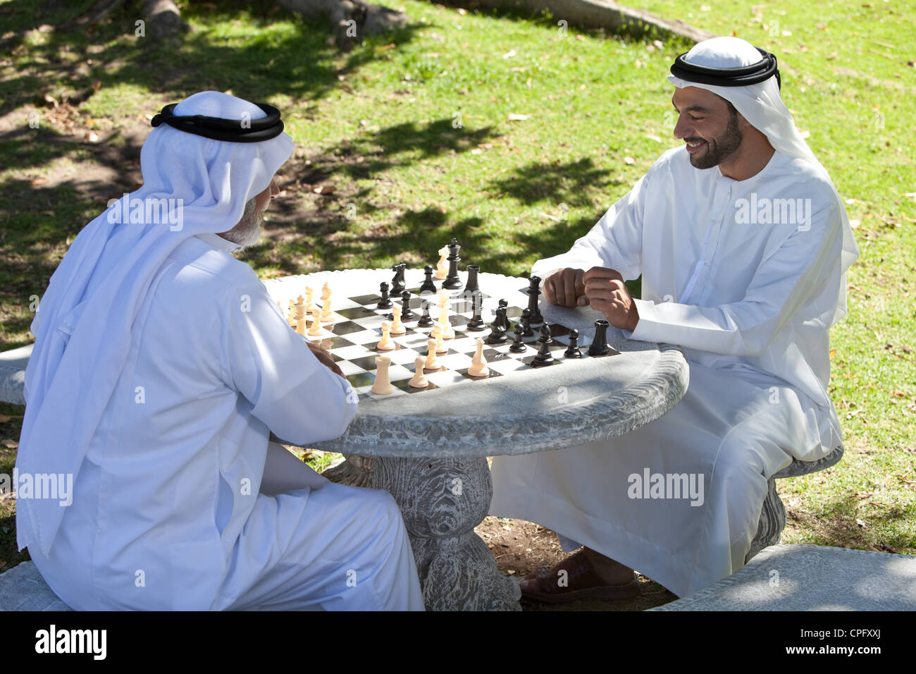 Fils adultes arabes jouant aux échecs avec le père dans le parc, en souriant. Banque D'Images