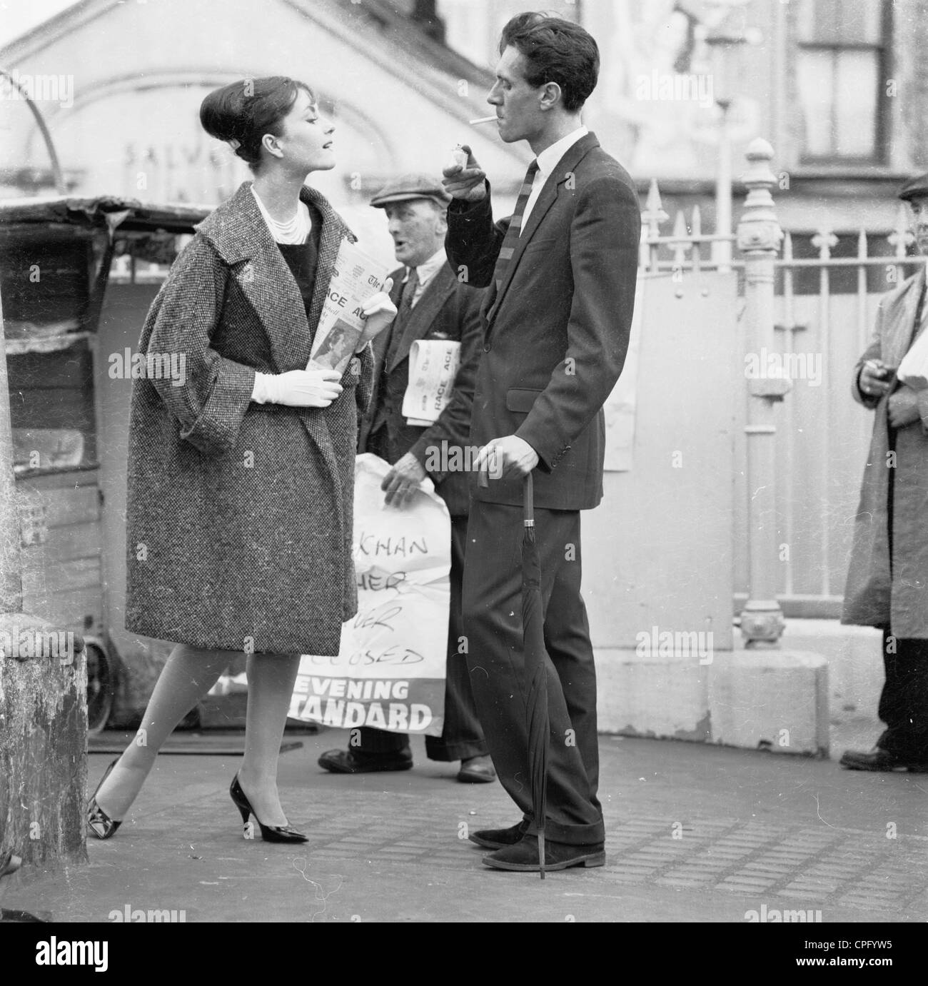 Se référant toujours à partir de 1960 montrant une jeune femme avec des fleurs avec un jeune homme fume une cigarette et s'appuyant sur un parapluie. Banque D'Images