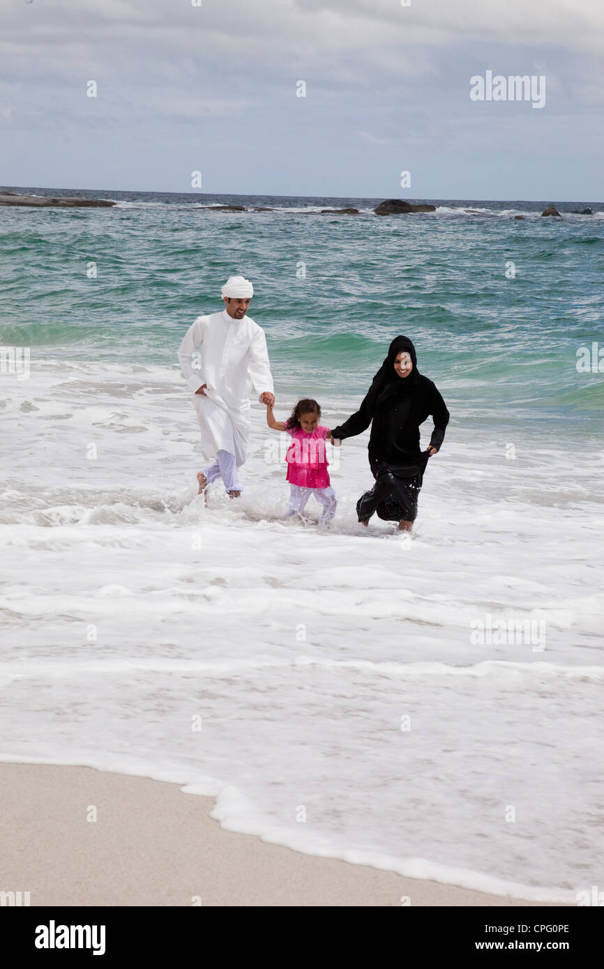 Famille arabe tenant la main tout en courant sur la plage. Banque D'Images