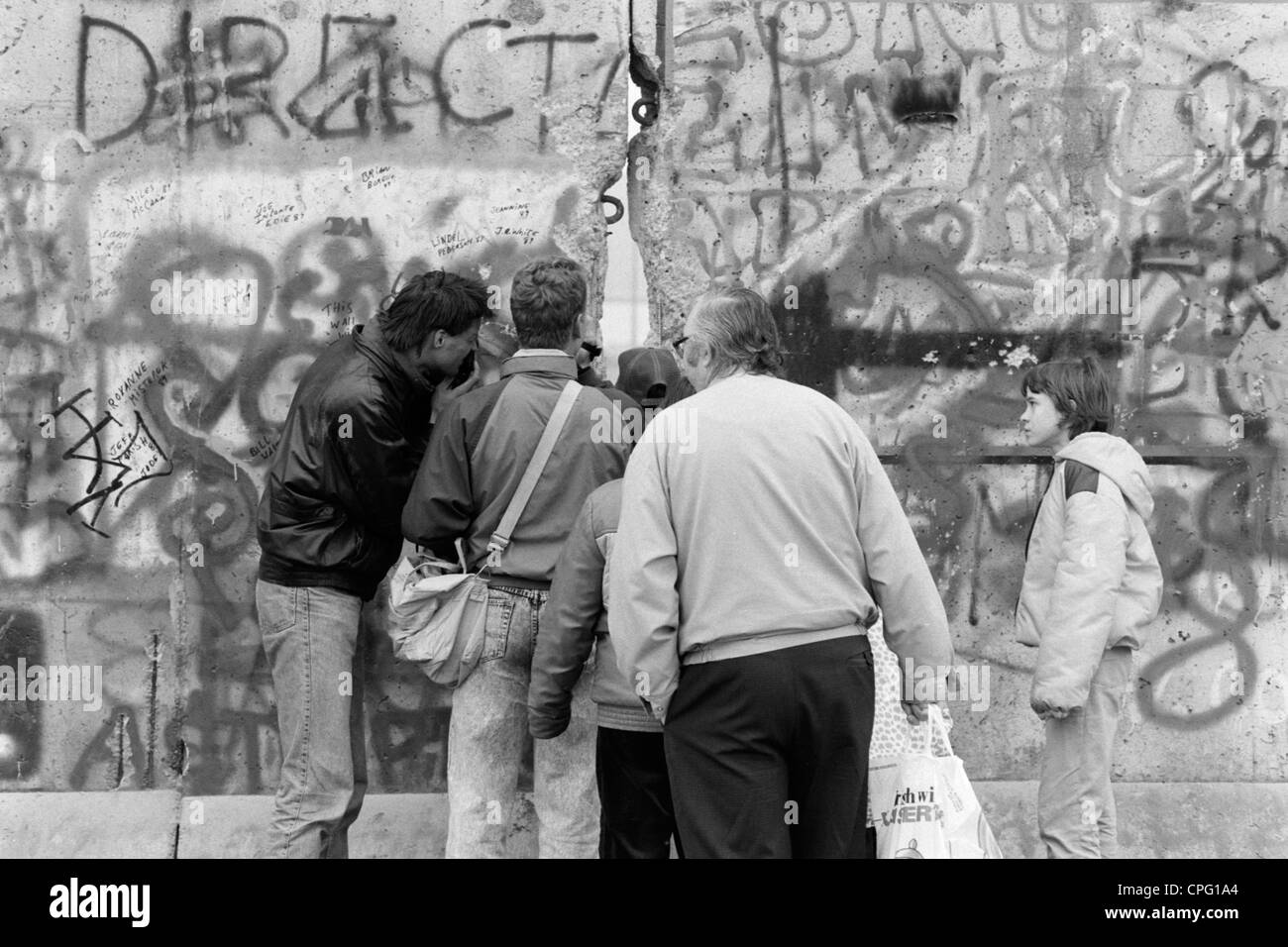 Les hommes à la recherche de la bande frontalière à travers un trou dans le mur de Berlin, Allemagne Banque D'Images