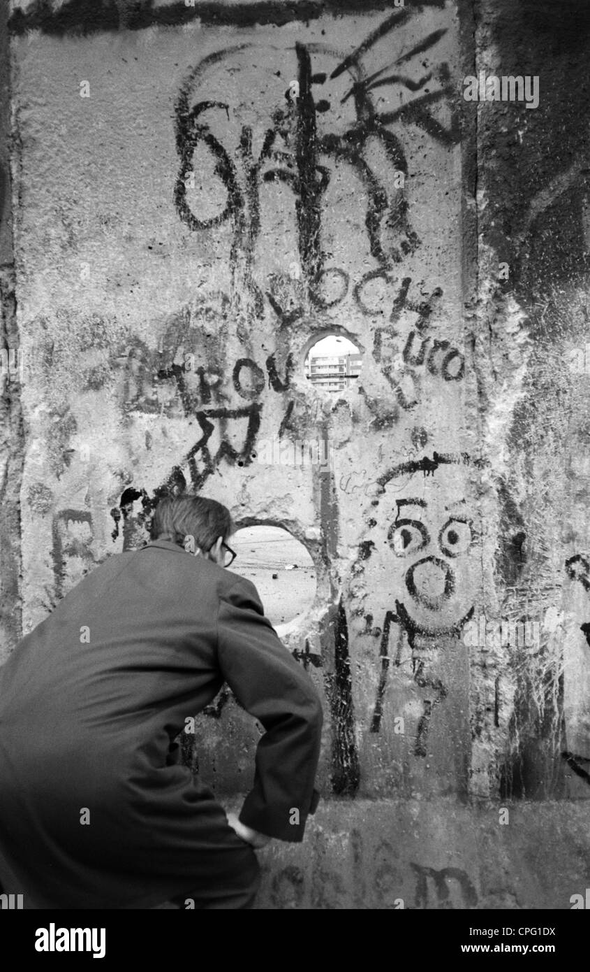 Un homme à la recherche de la bande frontalière à travers un trou dans le mur de Berlin, Berlin, Allemagne Banque D'Images