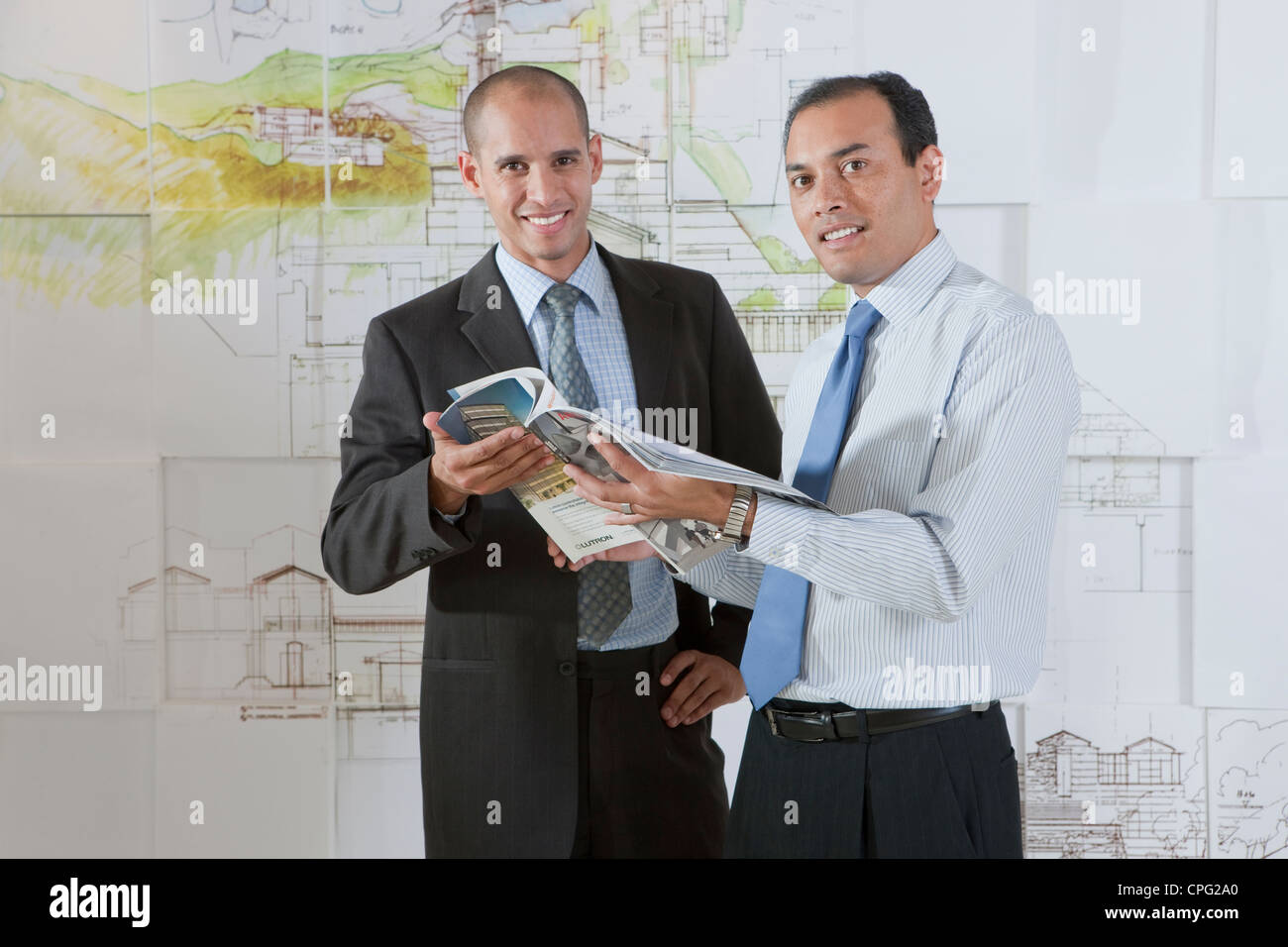 Deux hommes d'affaires avec l'article du magazine par le mur, souriant. Banque D'Images
