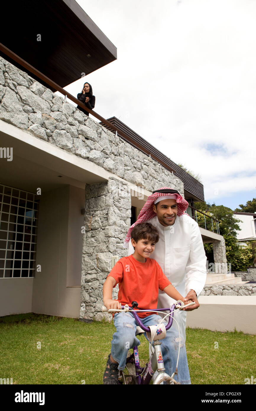 L'enseignement arabe père son fils comment monter à vélo, la mère à l'aide de téléphone mobile dans le balcon. Banque D'Images