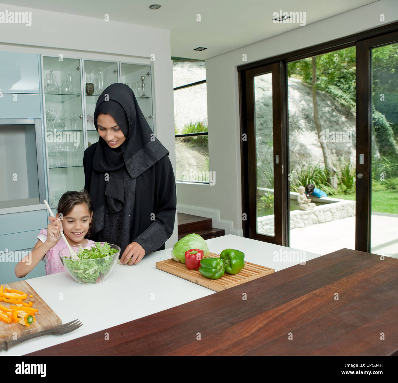 Fille de parents arabes avec la cuisson dans la cuisine, Garçon jouant à l'arrière-cour en arrière-plan. Banque D'Images