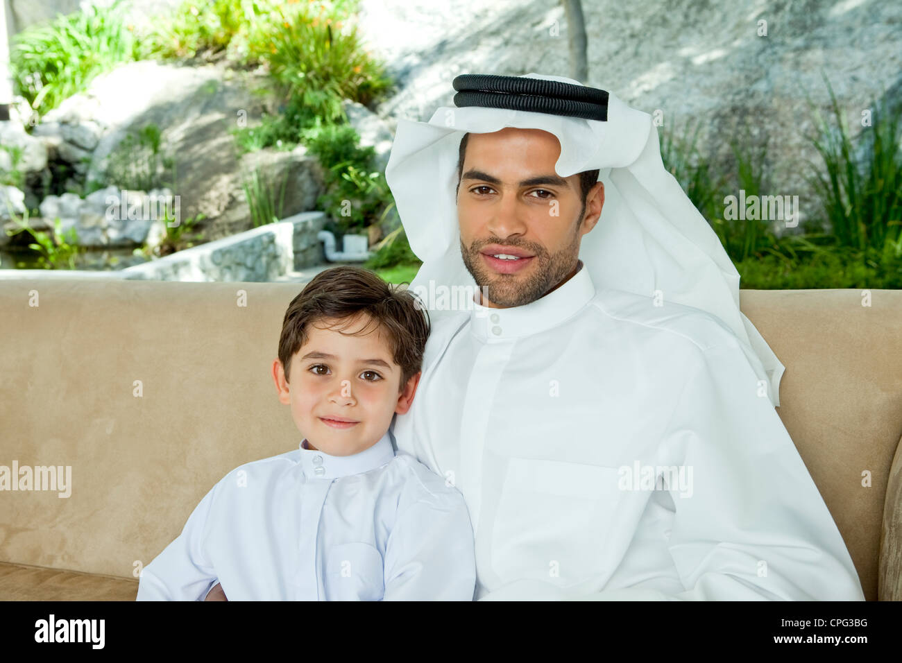 Portrait d'un père arabe et son fils assis sur le canapé, souriant. Banque D'Images