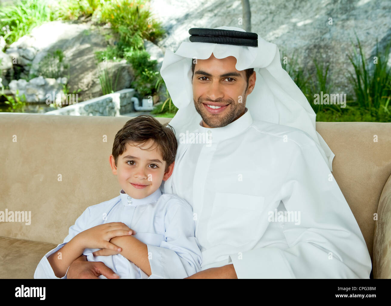 Portrait d'un père arabe et son fils assis sur le canapé, souriant. Banque D'Images