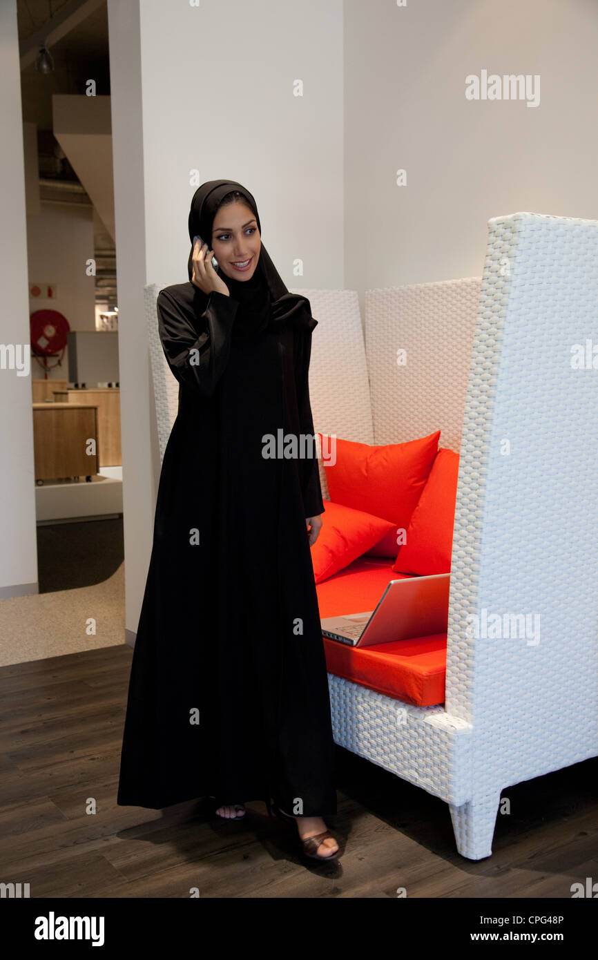 Femme arabe à l'aide de téléphone mobile, debout près du canapé. Banque D'Images