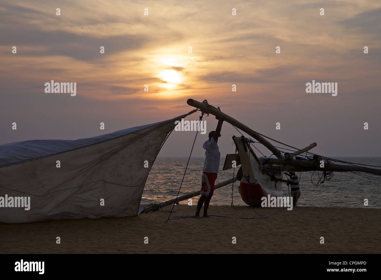 Pêcheur Prendre en bas la voile de son Oruvas, une pirogue à balancier, sur la plage de Negombo, Sri Lanka, Asie Banque D'Images