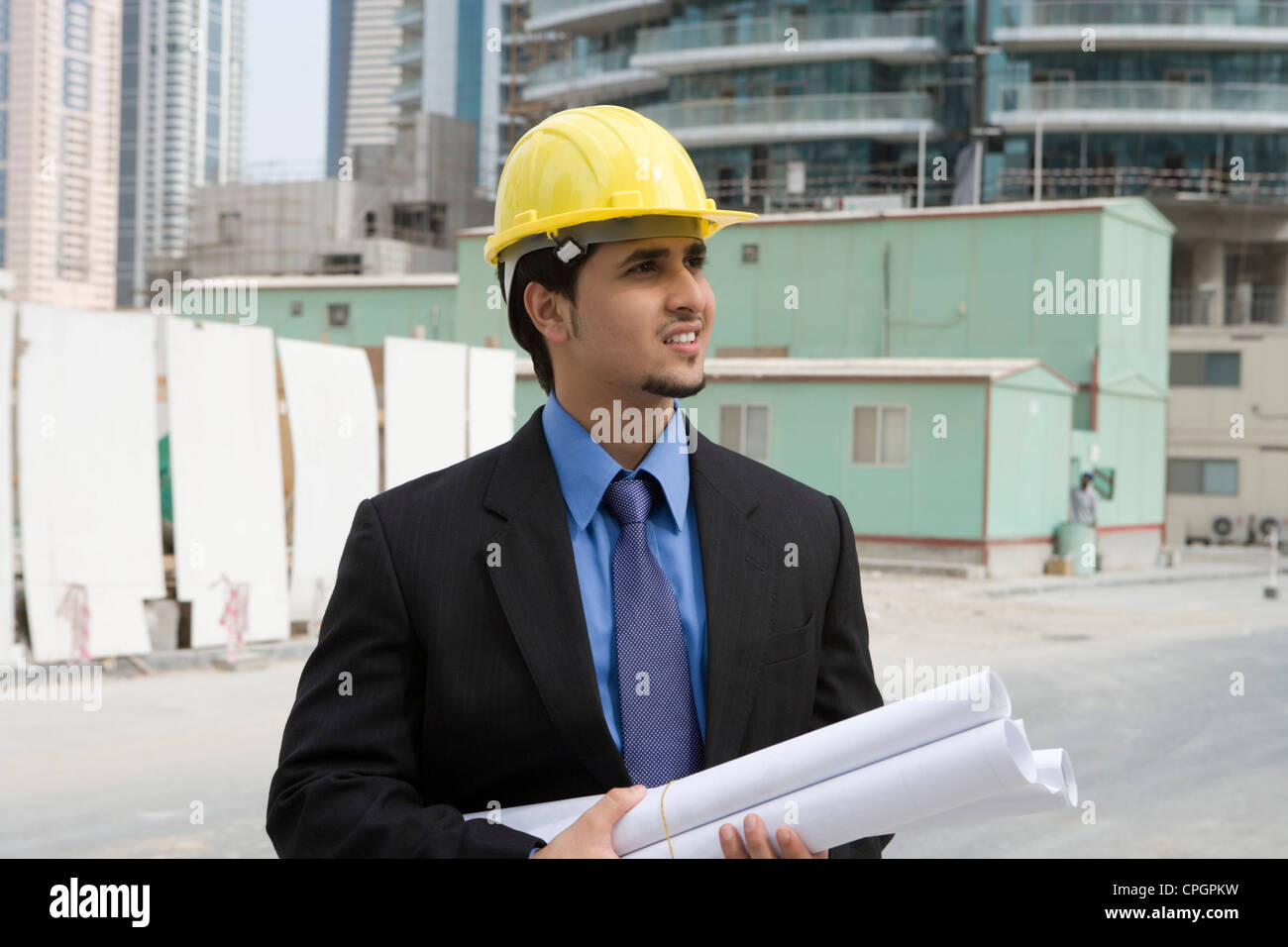 Businessman holding blueprints at construction site, smiling Banque D'Images