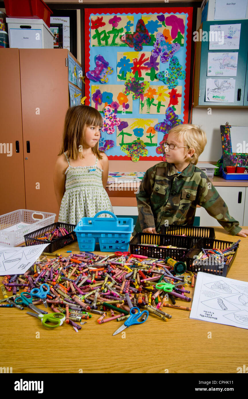 Les enfants de maternelle à San Clemente CA contempler une table pleine d'objets de classe y compris des crayons et des feuilles de Banque D'Images