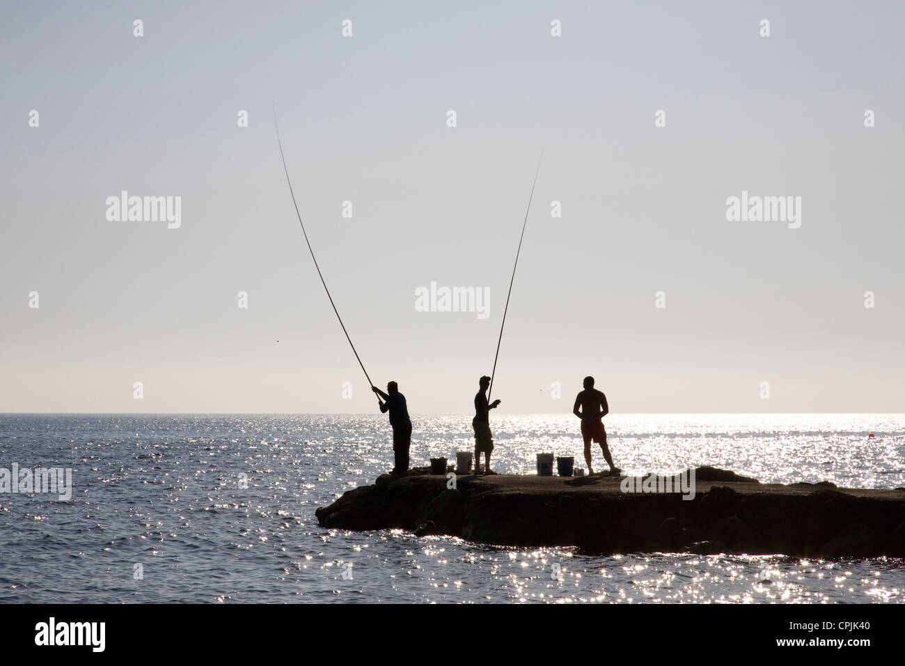 Les hommes pêche en mer à partir d'une jetée à plage de Kefalos, Paphos, Chypre. Banque D'Images