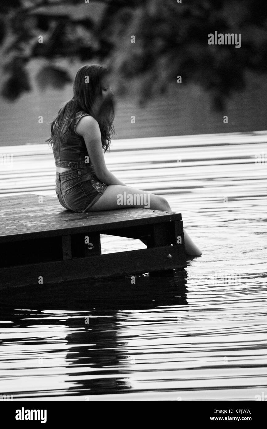 Belle jeune fille assise avec ses pieds dans le lac de s'éclabousser dans l'eau Banque D'Images