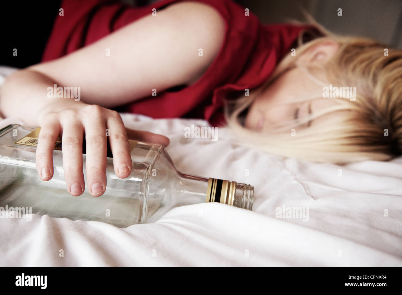 Drunken adolescente endormie sur un lit serrant une bouteille. Banque D'Images