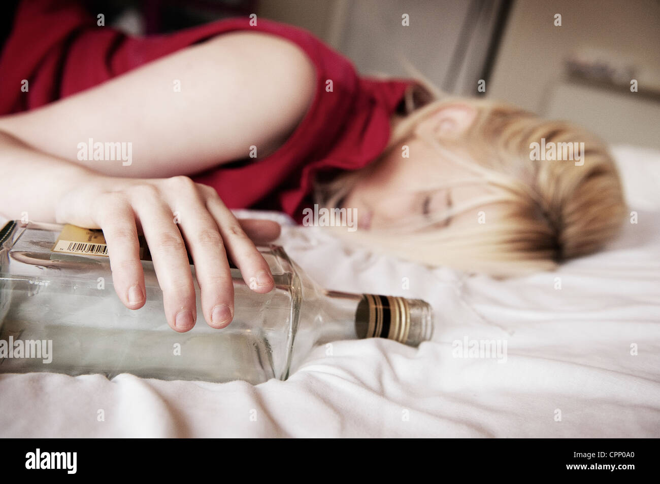 Drunken adolescente endormie sur un lit serrant une bouteille. Banque D'Images