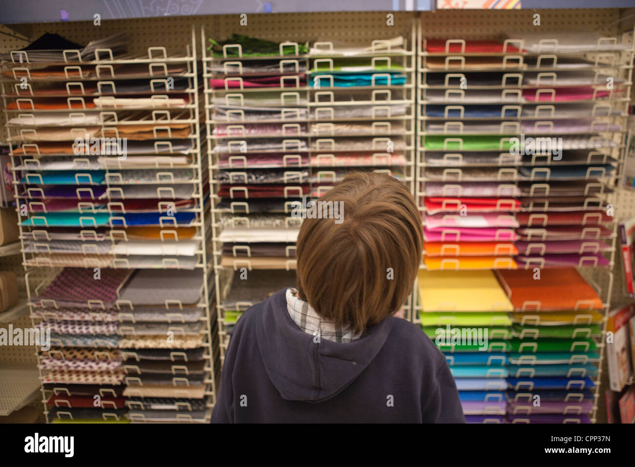 Un garçon de neuf ans à une sélection de la couleur du papier dans un magasin d'artisanat. Banque D'Images