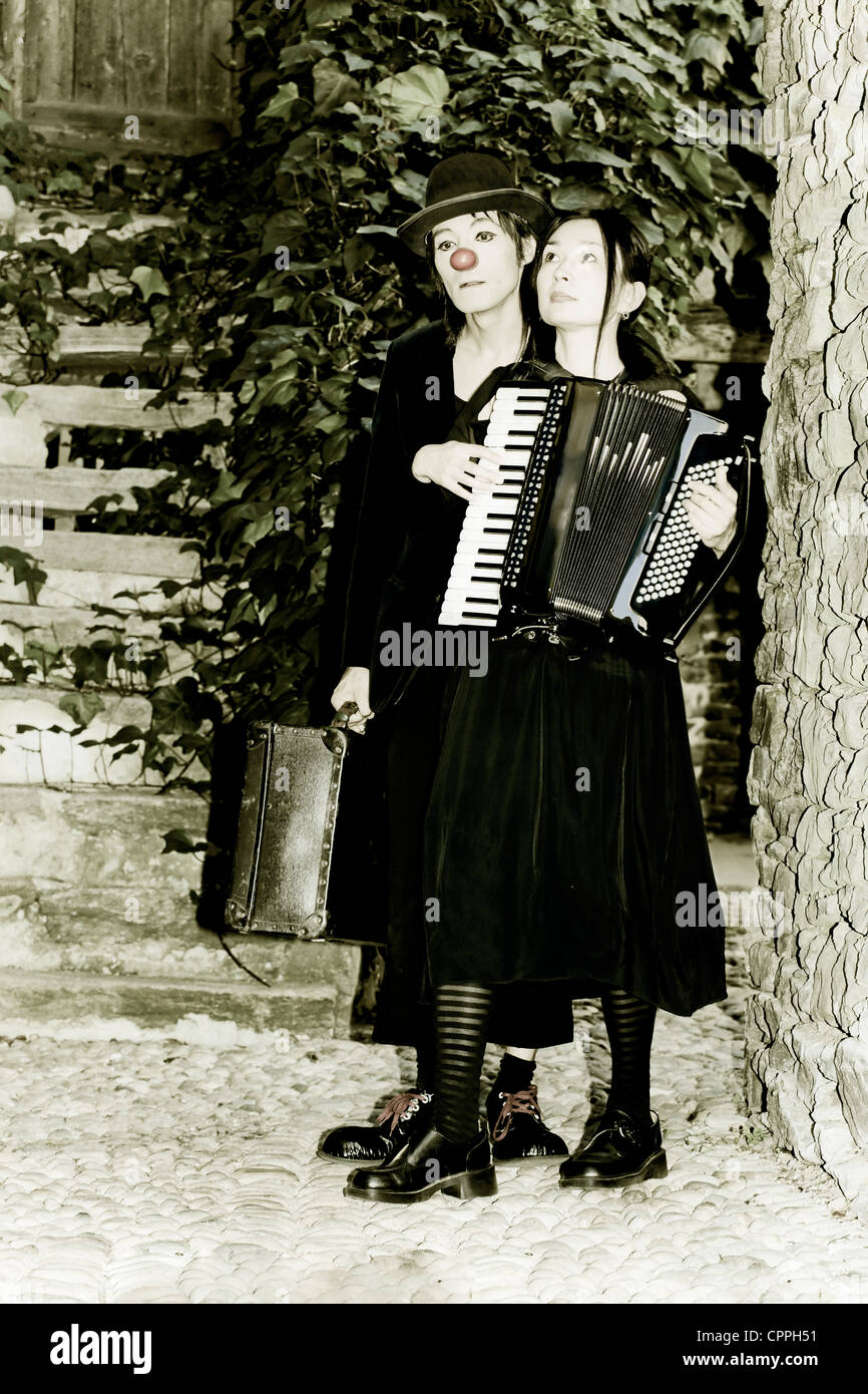 Un couple de clowns est balade au cœur d'un vieux, rue étroite, l'homme a une vieille valise, la femme joue de l'accordéon Banque D'Images
