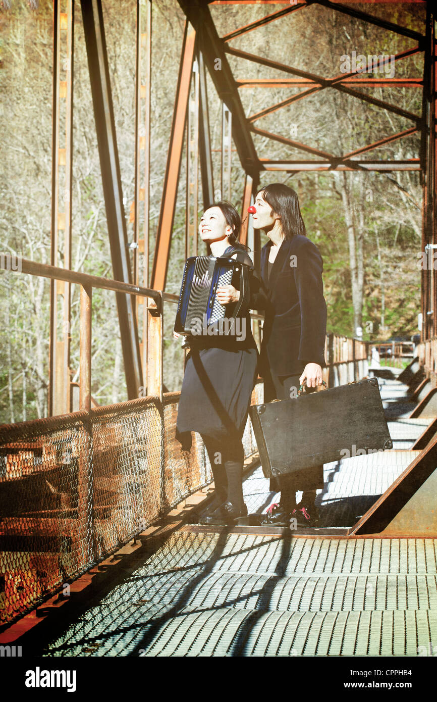 Un couple de clowns debout sur un vieux pont de chemin de fer, la femme jouant de la musique sur un accordéon Banque D'Images