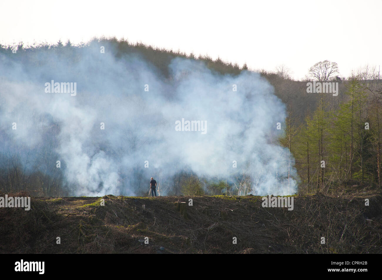 Un homme est tout juste visible contre la fumée des incendies de végétation et de broussailles brûler couper vers le bas lors de l'effacement de la zone de terre. Banque D'Images