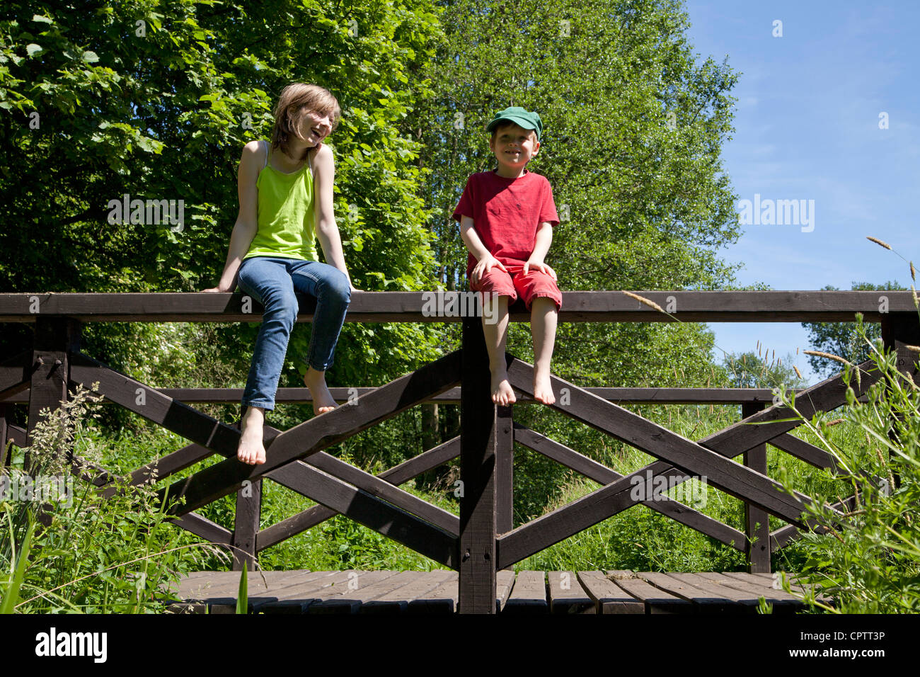 Fille et garçon assis sur la rambarde d'un pont en bois Photo Stock - Alamy