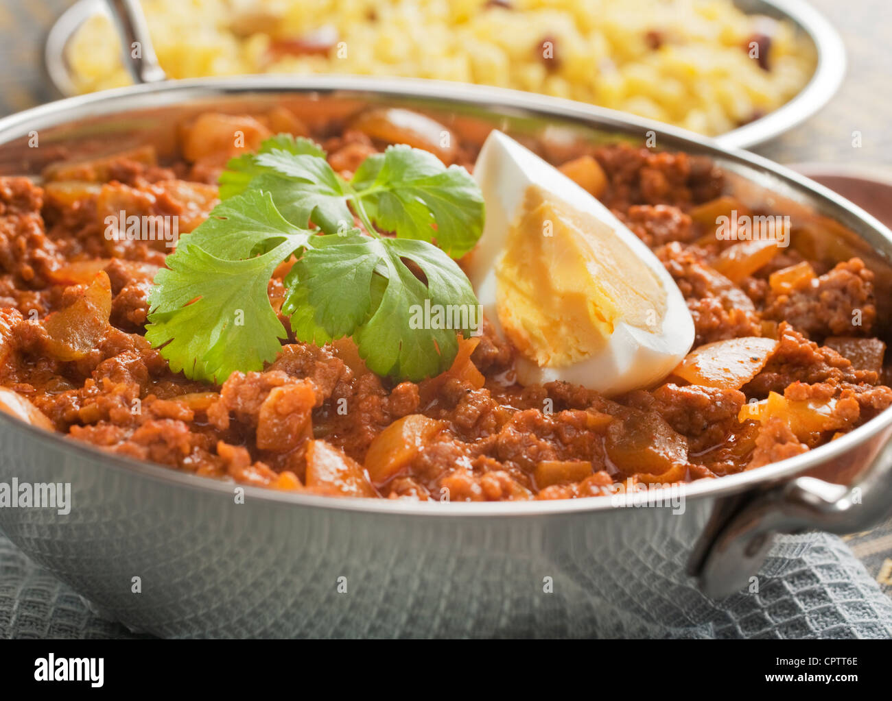 Boeuf keema curry à l'indienne, avec des œufs, dans un plat de Balti, garni de coriandre, avec du riz pilaf. Banque D'Images