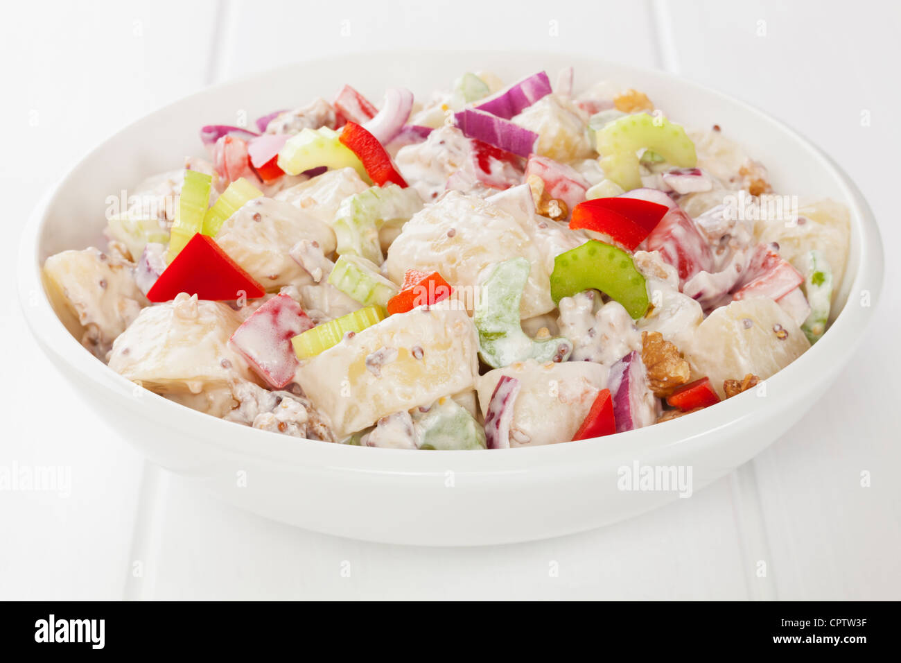 Salade de pommes de terre et de poivron rouge, oignon rouge, le céleri et les noix dans un miel moutarde, mayonnaise, sur un tableau blanc. Banque D'Images