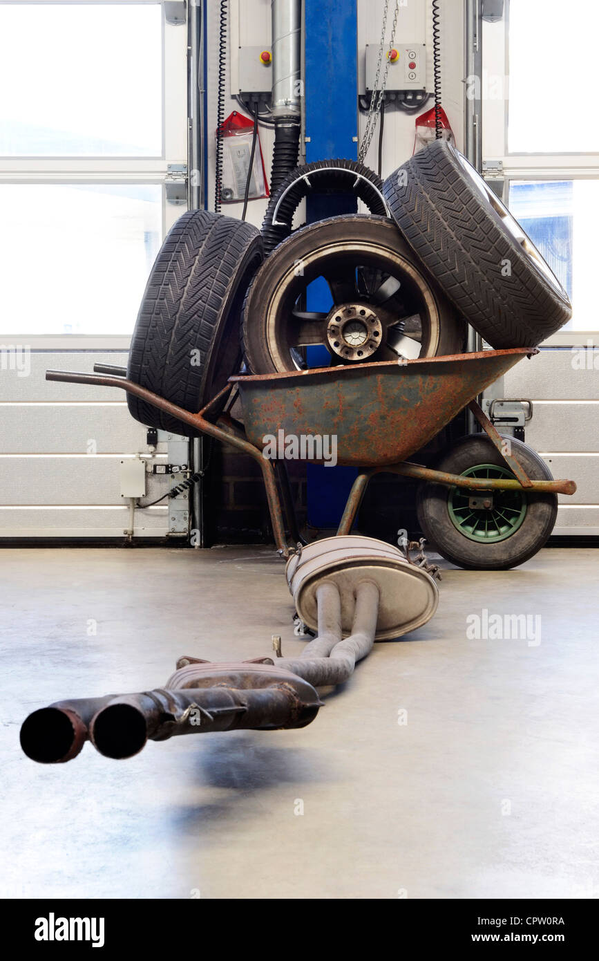 Brouette avec différentes roues et un système de silencieux d'échappement, et des pneus en face de deux portes de garage à un atelier de mécanique Banque D'Images