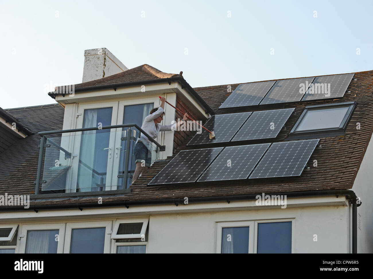 Nettoyer la poussière de sa femme panneaux solaires avec un balai sur le toit de la maison, promenade Sussex UK Banque D'Images