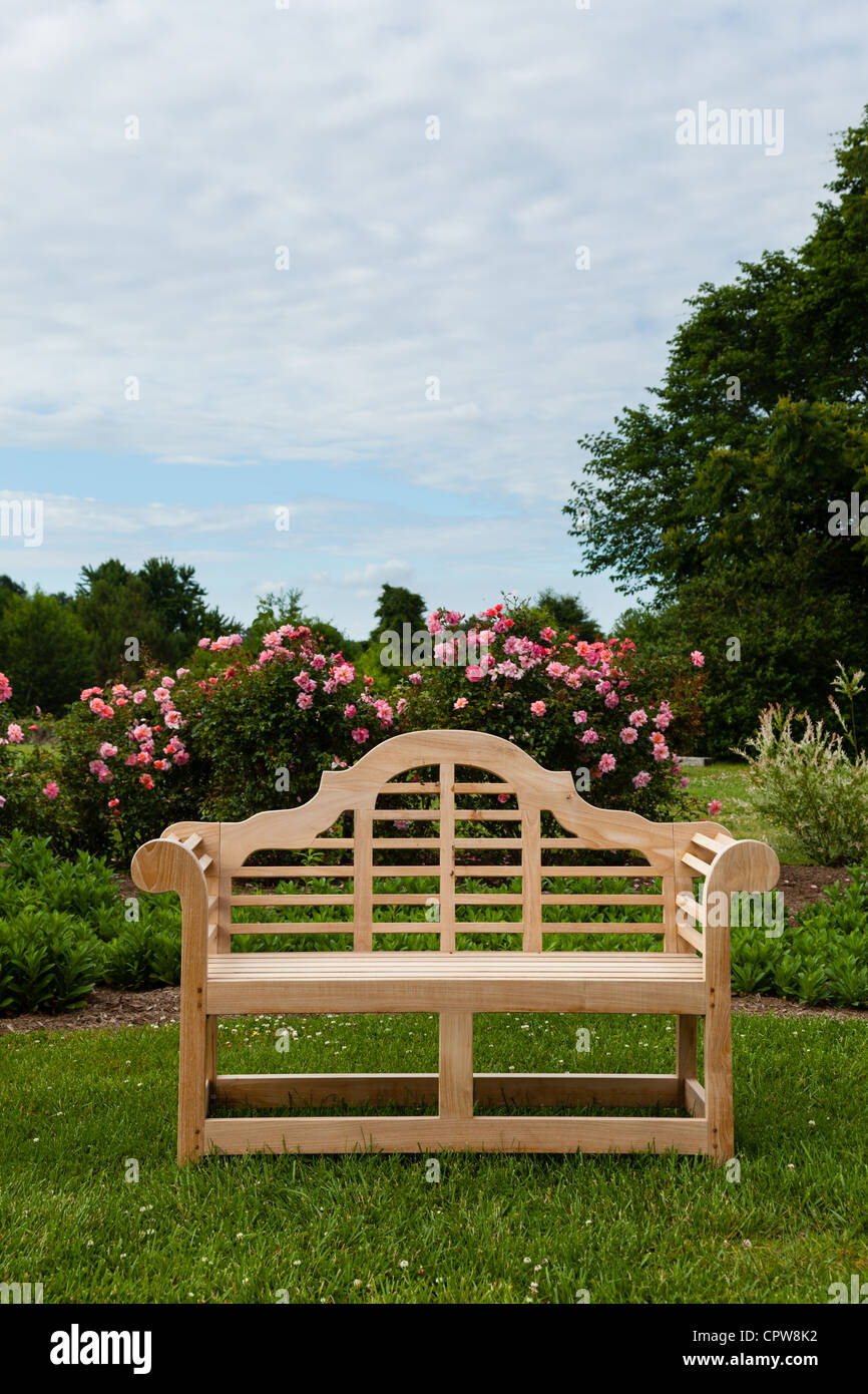 Banc sculpté en teck sur pelouse par lit de fleur avec des roses Banque D'Images