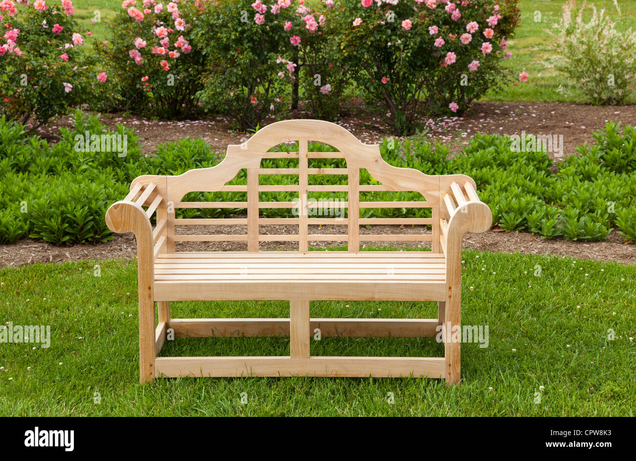 Banc sculpté en teck sur pelouse par lit de fleur avec des roses Banque D'Images